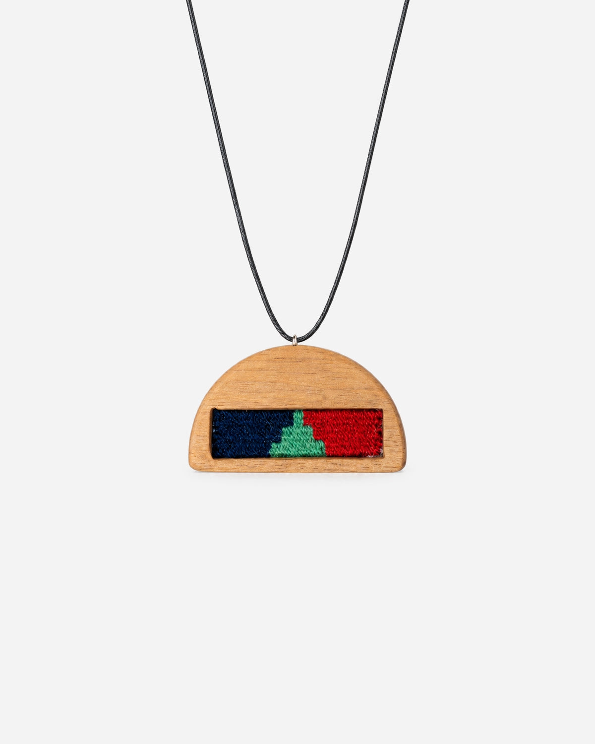 Crimson Dusk Kilim Necklace with navy, green and red weaving in a half-moon walnut frame on a black cord.
