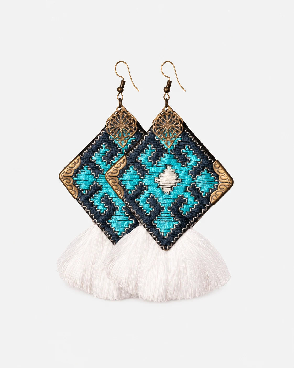 Turquoise Tradition diamond-shaped earrings with turquoise and dark woven patterns, gold-tone details and white fringe.
